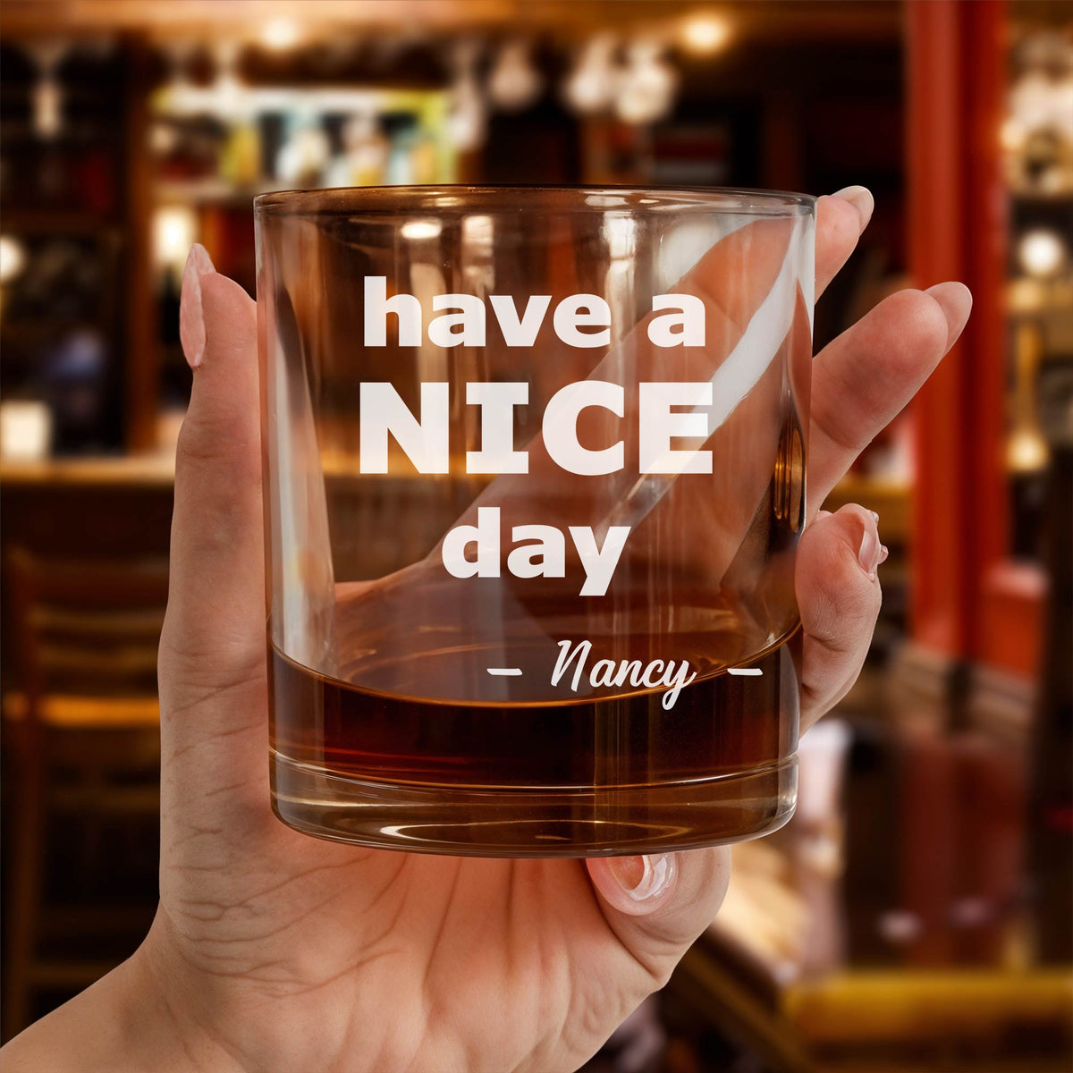 Personalized Whiskey Glass held in hand engraved with have a NICE day Nancy text in bar setting