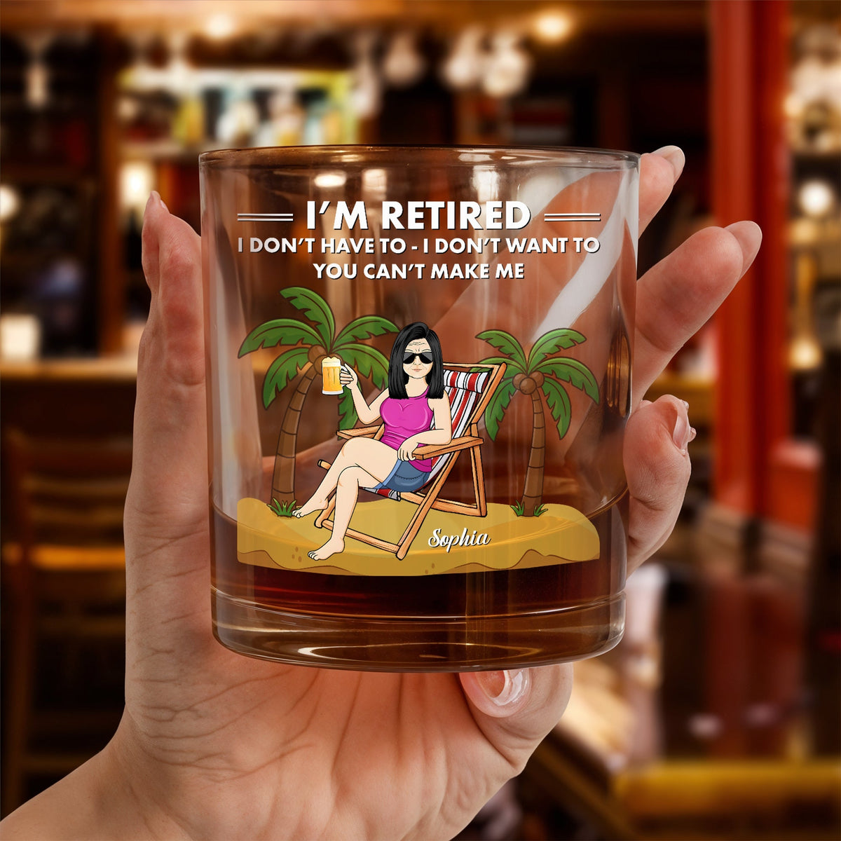 Personalized Whiskey Glass held in hand showing retired woman lounging on beach chair with palm trees and name Sophia