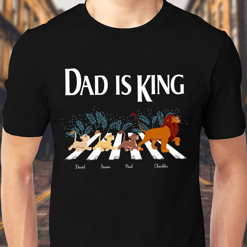 Black dad lion king shirt with cartoon lions crossing a street and text Dad is King