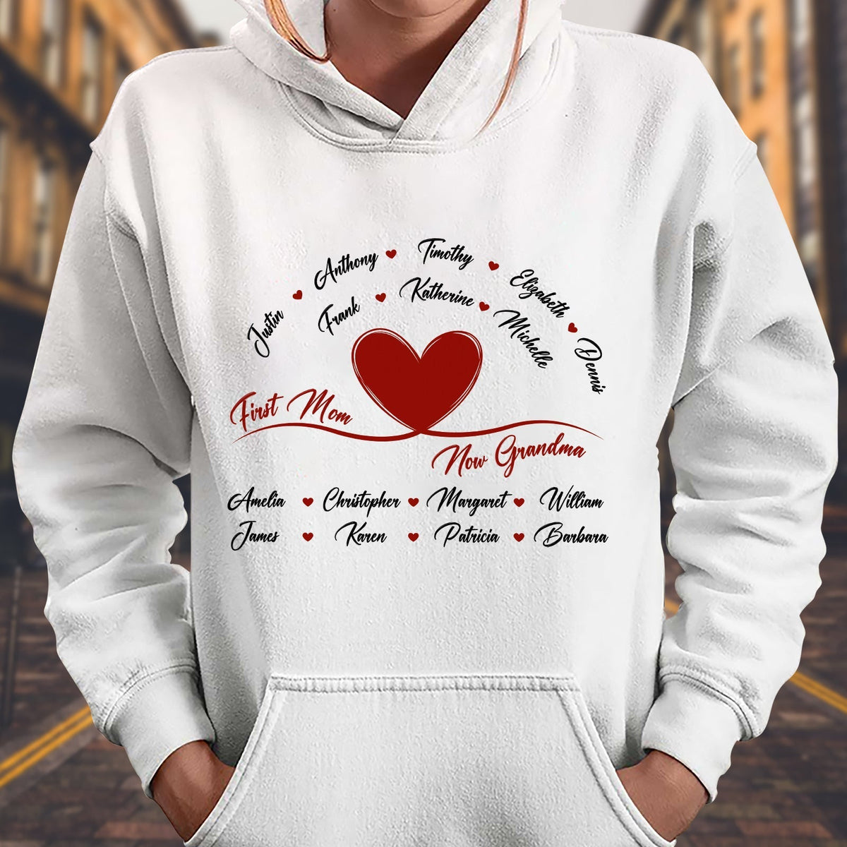 White hoodie with a red heart and personalized names design featuring first mom now grandma gift message