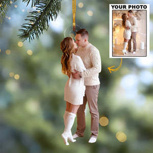 Personalized couple photo ornament hanging on Christmas tree branch with a cozy couple in winter attire