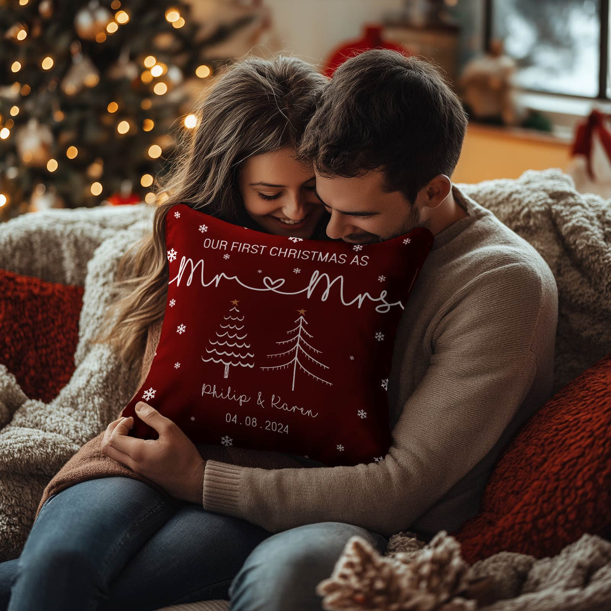 Couple hugging a personalized first Christmas pillow with names and date in a cozy festive living room