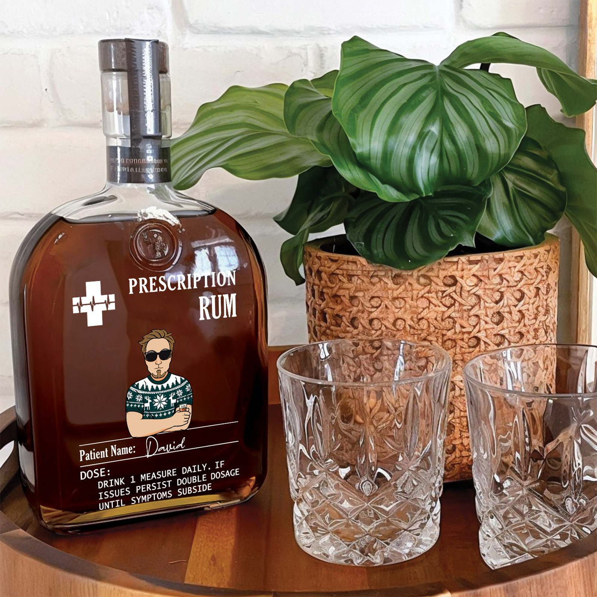 Personalized prescription whiskey bottle with custom label beside two crystal glasses and a plant